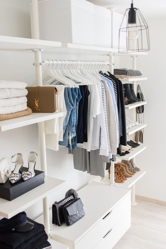 a minimalist closet with lots of open shelves, a dresser and lots of white clothes hangers plus boxes overhead