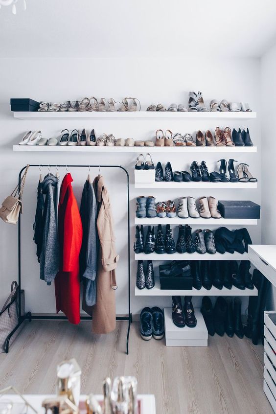 a minimalist closet with lots of open shelves for shoes, a dresser and a black holder for clothes hangers