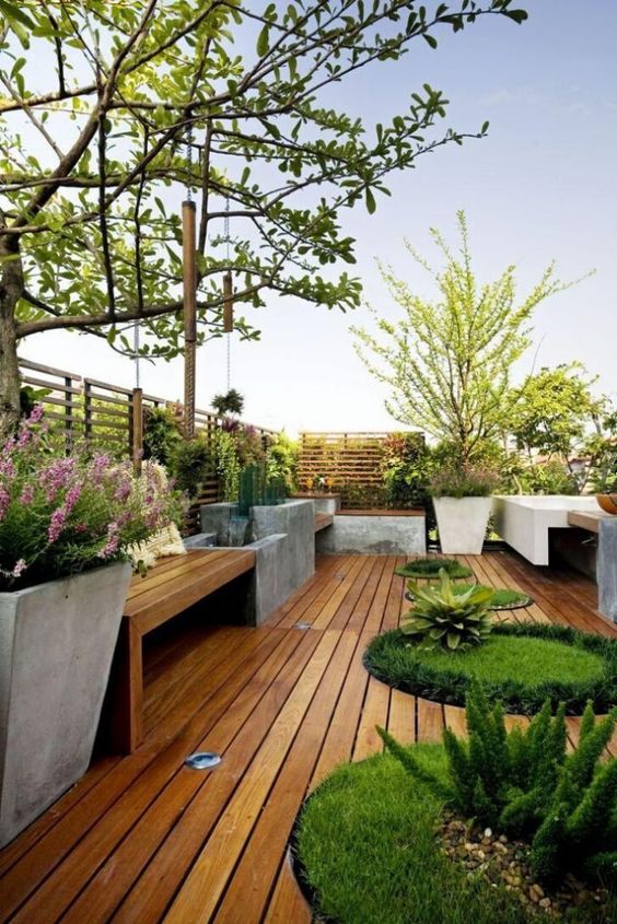 a minimalist deck with built-in benches and concrete planters, round built-in flower boxes with greenery and trees and blooms is like a super-modern garden