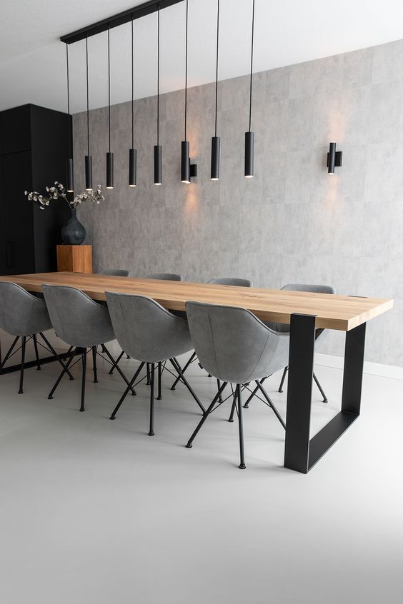 A minimalist dining space with a long light stained table, grey chairs, a cluster of black tube pendant lamps and sconces