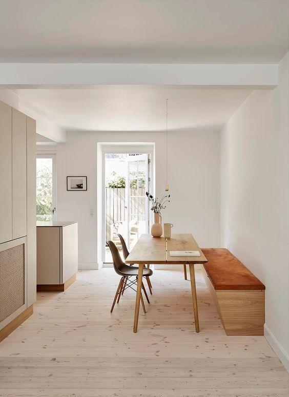 a minimalist dining space with an upholstered bench, a stained table and black Eames chairs and a pendant lamp