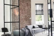 a minimalist living room with a brick wall, a grey sofa, a black coffee table and black shades