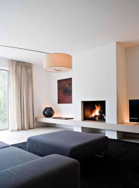 a minimalist living room with black furniture and a rug, a fireplace, an artwork, a lamp and neutral curtains