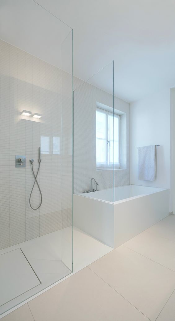 a minimalist neutral bathroom with largre scale and skinny tiles, a glass enclosed shower and a soak tub