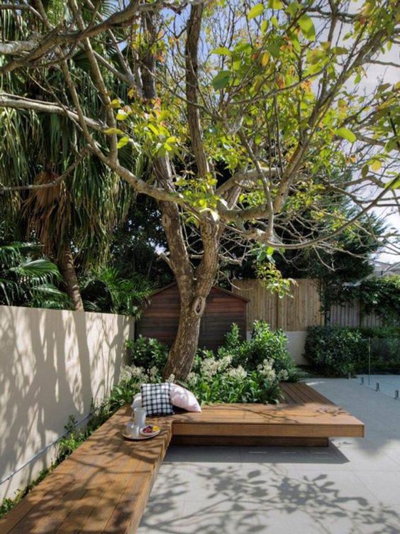 a minimalist terrace clad with concrete tiles, with a built-in bench, some greenery and trees growing here is a lovely space to have a rest
