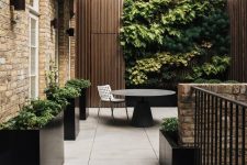a minimalist terrace clad with large scale tiles, black planters with greenery, a black round table, a living wall that makes a statement