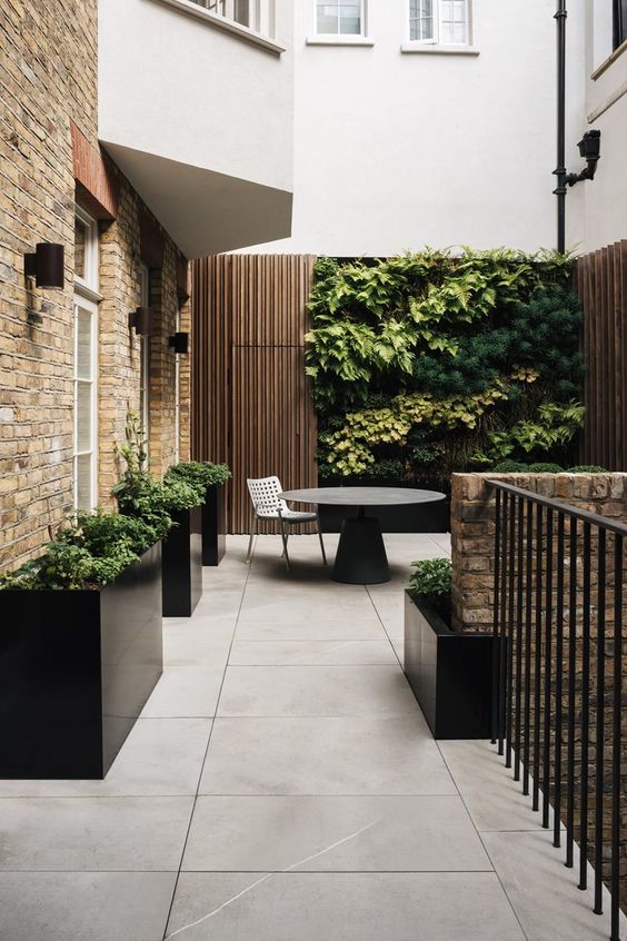 a minimalist terrace clad with large scale tiles, black planters with greenery, a black round table, a living wall that makes a statement
