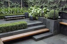 a minimalist terrace clad with stone tiles, a built-in bench, a black bench, planters and lots of greenery to make the space look fresh