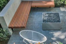 a minimalist terrace with concrete tiles, a built-in corner bench, a fire pit, a round chair and lots of greenery and blooms around