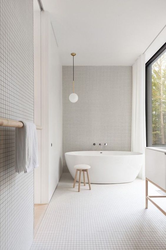 a minimalist white bathroom all clad with small white tiles, a glazed wall and white appliances