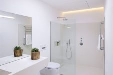 a minimalist white bathroom with a skylight and built-in lights, a sleek vanity, a shower with a glass partition and white appliances