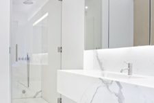 a minimalist white marble bathroom with a shower space, a floatign vanity, a statement mirror and built-in lights