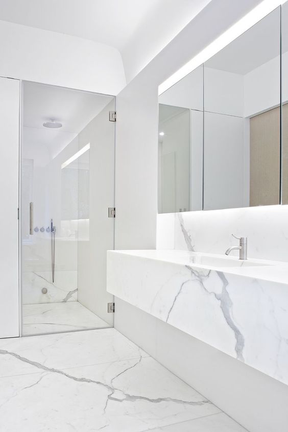 a minimalist white marble bathroom with a shower space, a floatign vanity, a statement mirror and built-in lights