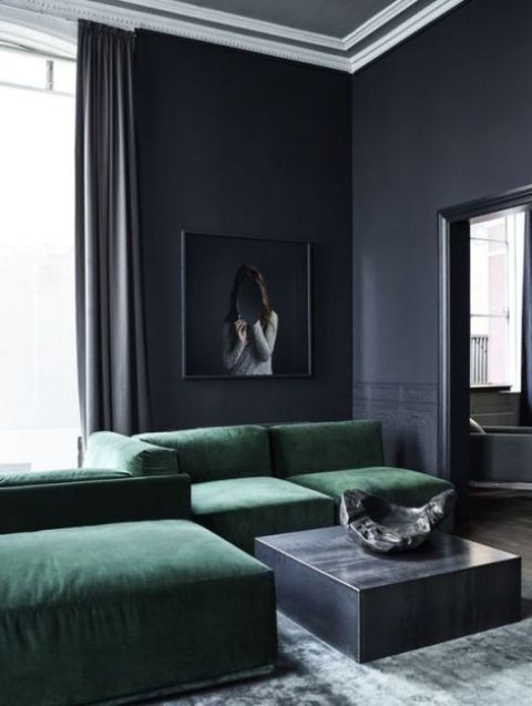 a moody graphite grey living room with a small coffeee tables, an emerald grene sectional sofa and a statement artwork