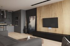 a moody minimalist living room with a wooden wall, a grey sofa, dark touches and an artwork plus a TV on the wall