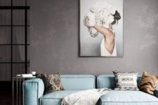 a moody minimalist living room with an aqua sofa, an artwork, a rug and chevron clad wooden walls