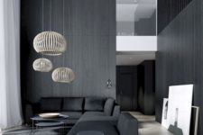 a moody minimalist living room with black walls and a sectional sofa, rattan lampshades and a couple of coffee tables