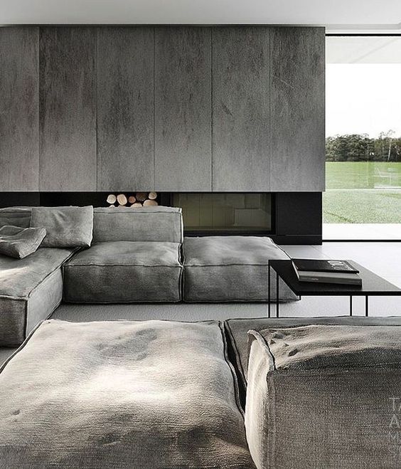 A moody minimalist living space with grey panels, a built in fireplace, grey canvas furniture and black touches