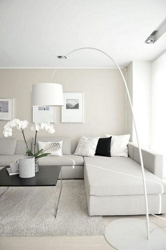 A neutral minimalist living room with an off white sectional sofa, a floor lamp, artworks and potted blooms