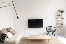 a neutral minimalist living room with off-white cushions, wooden furniture, a TV on the wall and a wall lamp