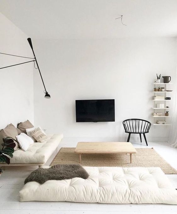 A neutral minimalist living room with off white cushions, wooden furniture, a TV on the wall and a wall lamp