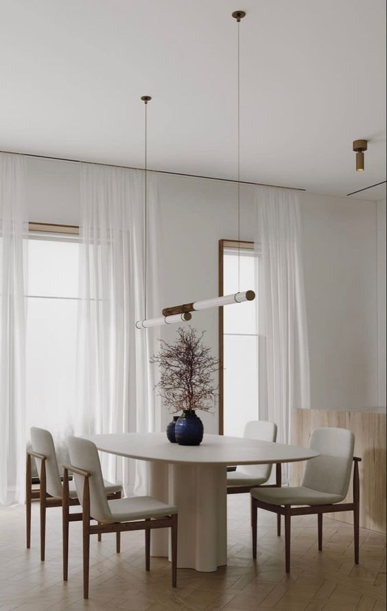 a pure minimal and airy dining room with an oval table, creamy chairs with stained frames and pendant tube lamps plus catchy branches in vases