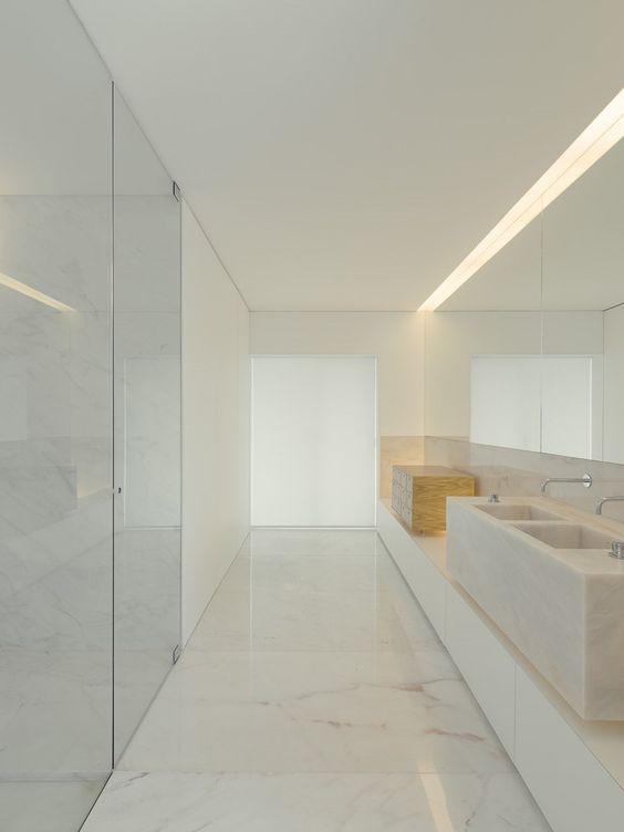 a pure minimalist bathroom done with white marble, a floating vanity, a stone slab sink and a shower clad with glass