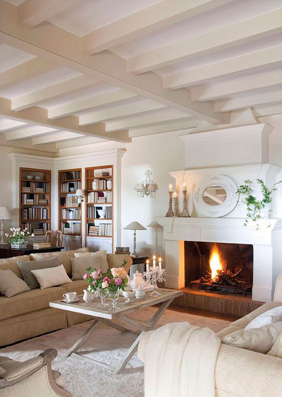 a romantic Provence living room with a fireplace, neutral furniture and a trestle table, candleholders and a mirror on the mantel
