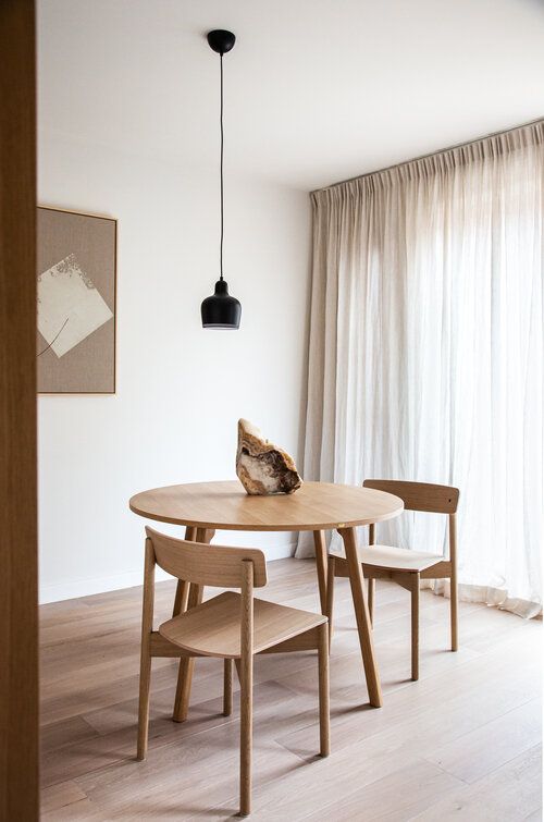 a simple and minimal dining space with a stained table and chairs, a black pendant lamp and a piece of rock for an accent