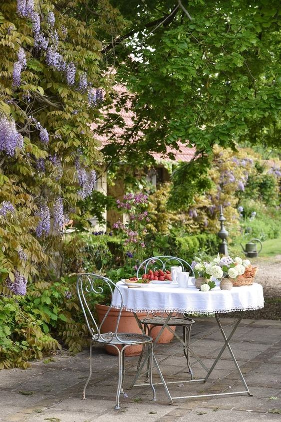 A small and lovely Provencal outdoor space with a metal table and chairs and some blooms and greenery around   who needs more than that