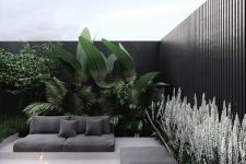 a stylish and ultra-minimalist terrace in neutrals, with black cushions and pillows, a fire pit, greenery and large plants is a very chic space