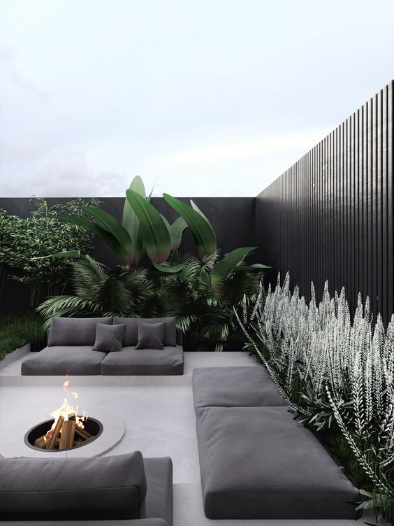 A stylish and ultra minimalist terrace in neutrals, with black cushions and pillows, a fire pit, greenery and large plants is a very chic space