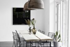 a stylish minimal dining space with a light-stained dining table and black metal chairs, brushed metal pendant lamps
