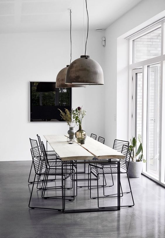 a stylish minimal dining space with a light-stained dining table and black metal chairs, brushed metal pendant lamps