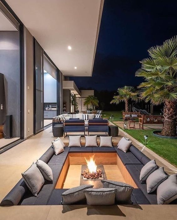 a stylish minimalist sunken fire pit with a built-in bench, lots of cushions and pillows and a fire pit in the center is a very chic idea