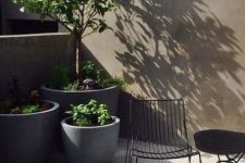 a tiny minimalist terrace with geo tiles, concrete planters with greenery and trees, a black table and a black chair