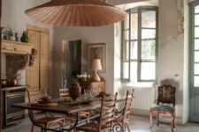 a vintage kitchen and dining space in one, with rich-stained wooden beams, a refined dining table and stained chairs, a wicker pendant lamp and some furniture