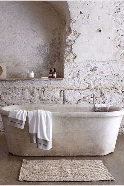 A wabi sabi bathroom in neutrals with stone wall, a stone tub and a jute rug looks very roough and imperfect