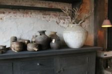 a wabi-sabi space with a rough brick wlal, a wooden cabinet, some rough stone vases and planters