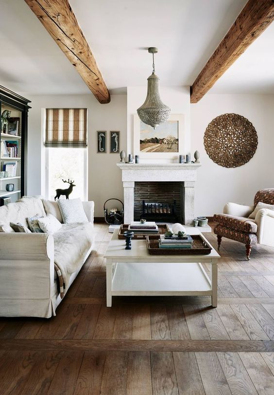 a welcoming Provence living room with a fireplace, neutral furniture, wooden beams and a low coffee table plus a bookcase