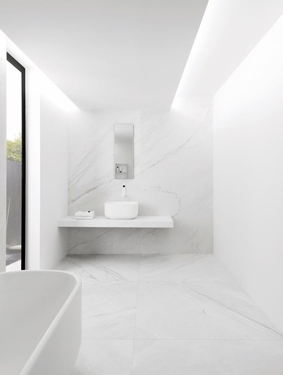 a white minimalist bathroom with a large window, a floating vanity, a bowl sink and a bathtub plus white marble