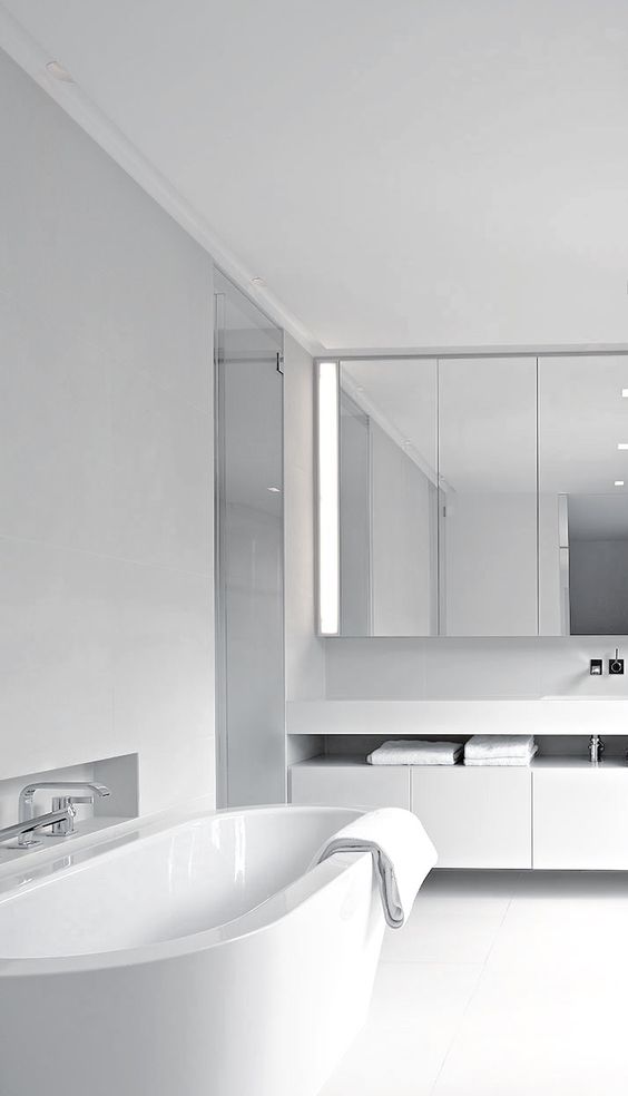a white minimalist bathroom with a mirrored cabinet, a floating vanity, a white tub, stainless steel fixtures