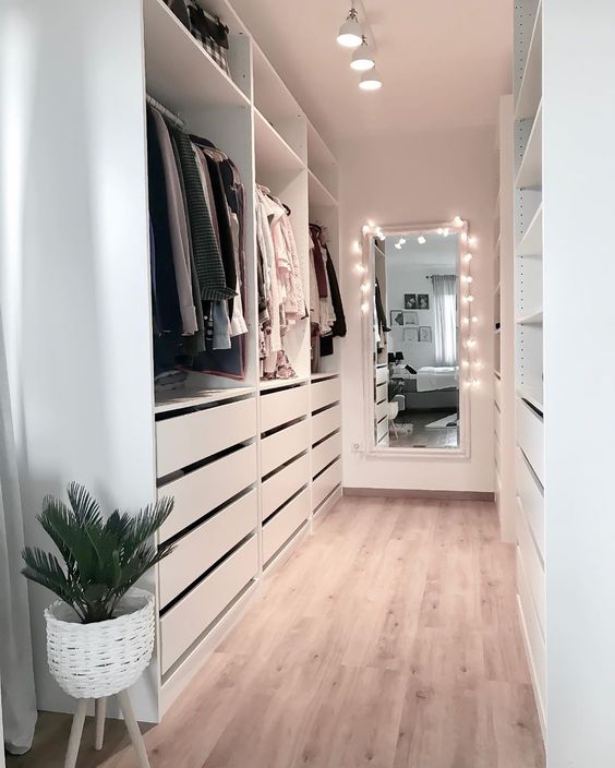 a white minimalist closet with drawers, open shelving and holders plus a mirror with lights to see what to wear