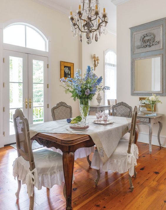an exquisite French chic dining room with a stained vintage table, grey vintage chairs, a mirror, a whitewashed console table and a vintage chandelier