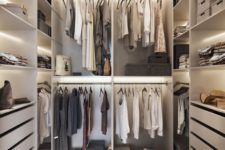 an ivory minimalist closet with built-in lights, drawers, open shelves and open holders for hangers