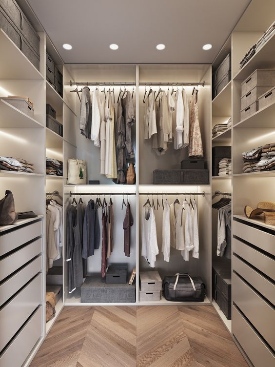 An ivory minimalist closet with built in lights, drawers, open shelves and open holders for hangers