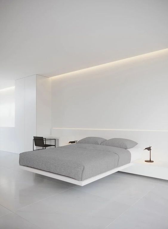 An ultimately minimalist bedroom in white, wiht a built in floating bed, built in nightstands and a desk, black floor lamps
