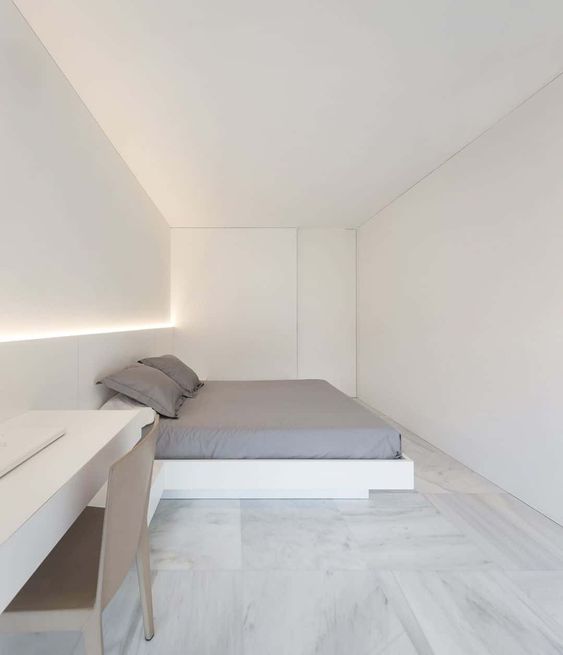 An ultra minimalist white bedroom with a bed, built in lights, a built in desk and a plywood chair is cool