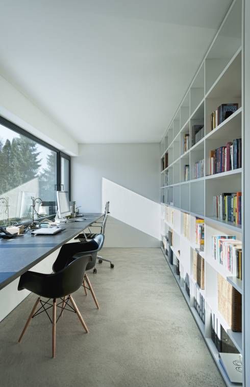 a Nordic home office with a long and narrow window, a windowsill shared desk, black chairs and a large bookcase as a space divider
