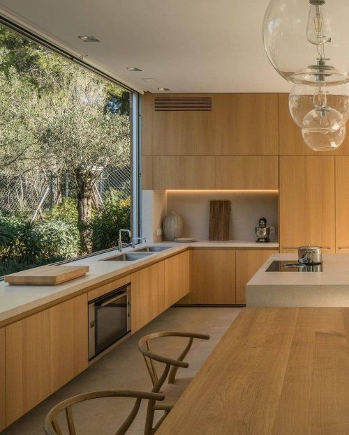 a beautiful contemporary kitchen with sleek light-stained cabinets, white stone countertops, built-in lights and a glazed wall with garden views
